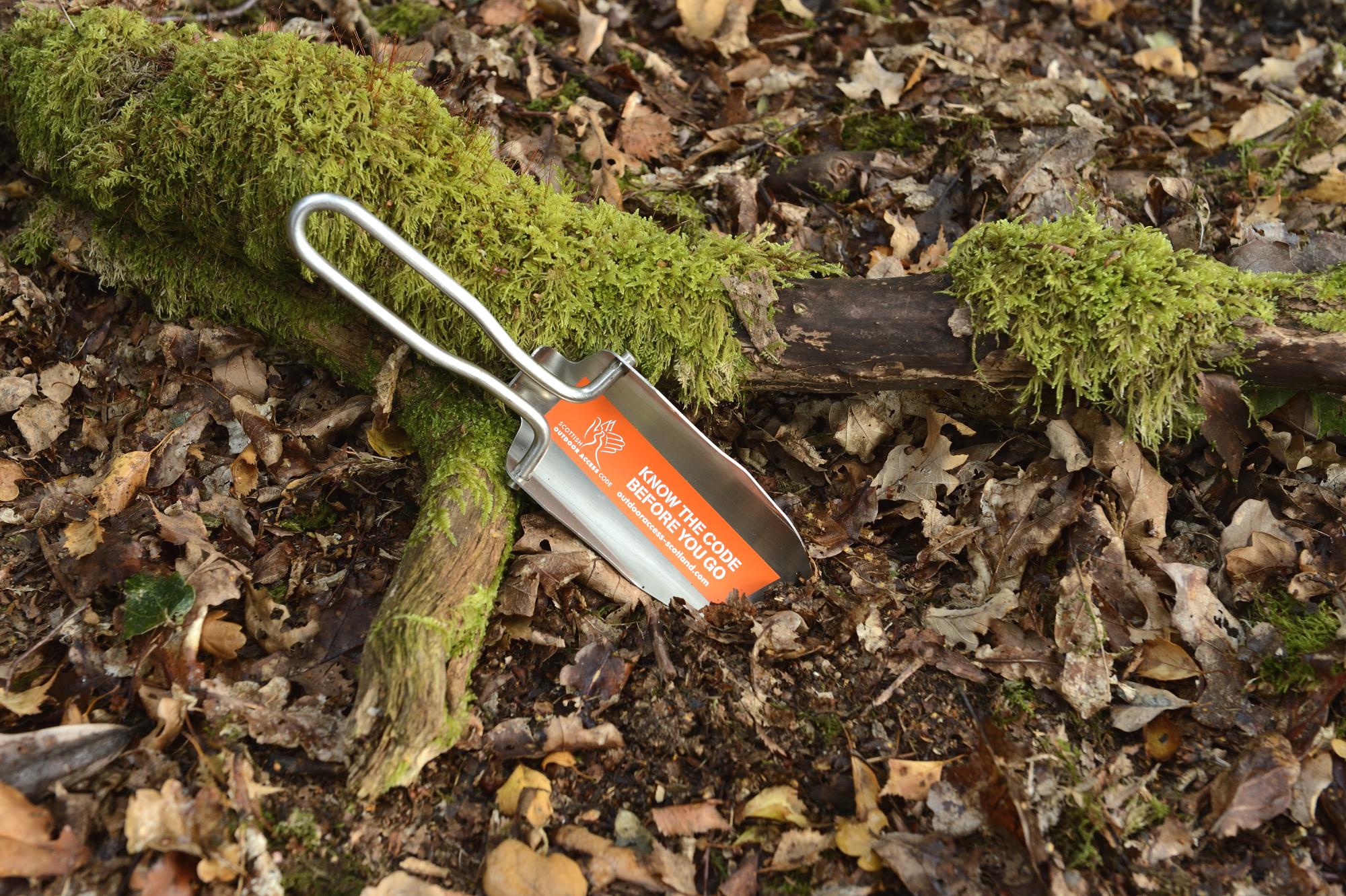 Photo of a 'Know the code before you go' trowel in leaf litter next to tree roots. ©Lorne Gill/NatureScot
